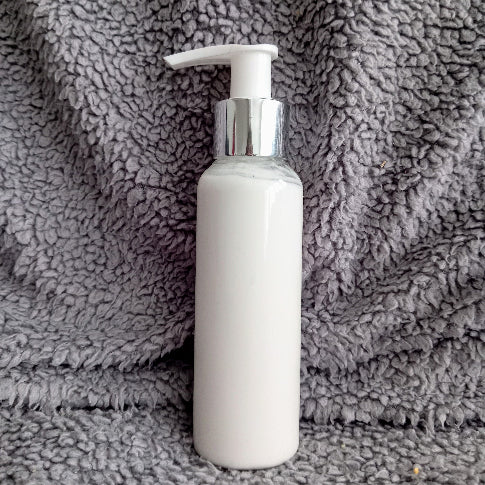 White Body lotion bottle with pump on a grey textured surface Four candles and soaps