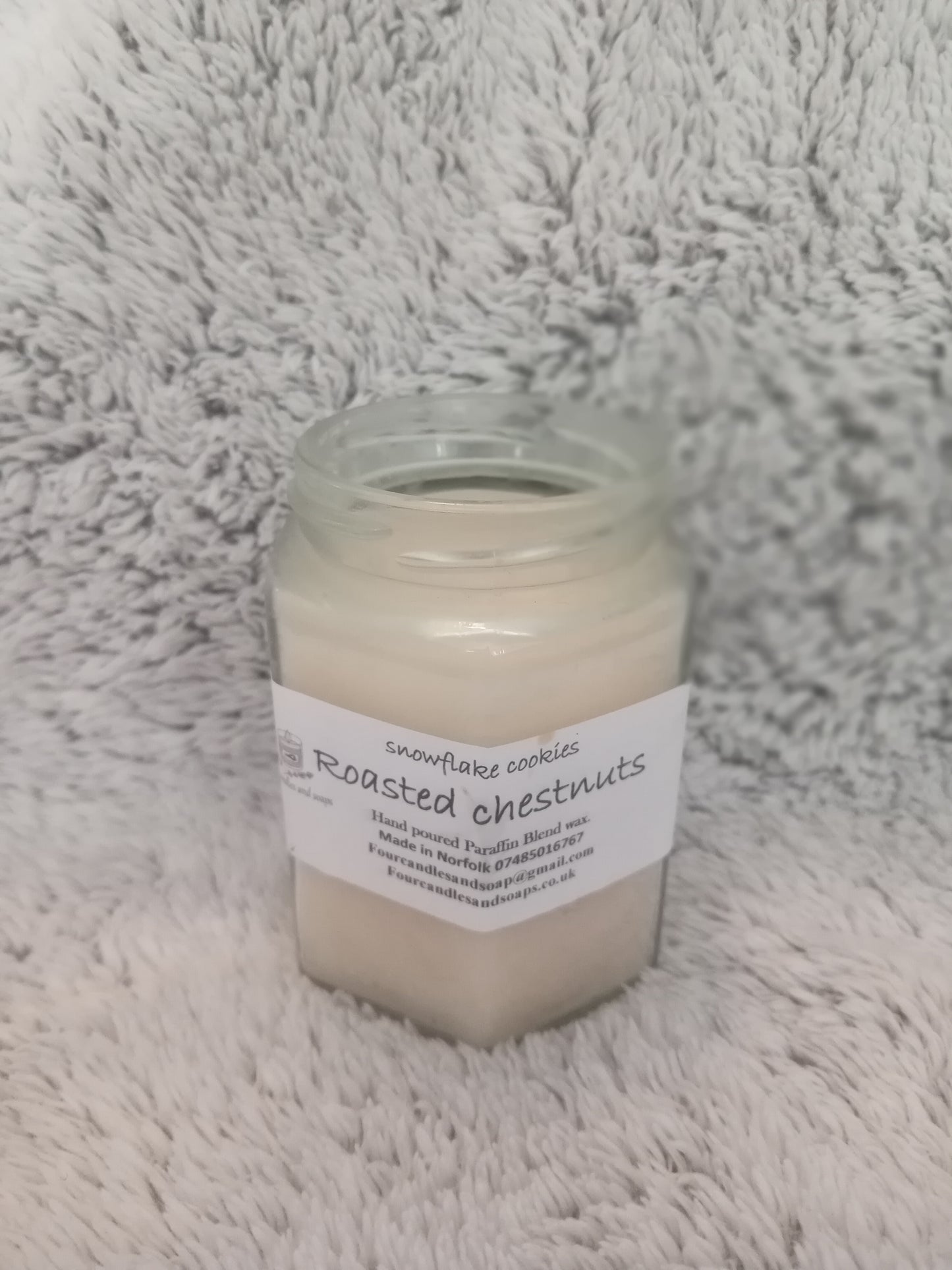 A jar candle with a label that reads 'Roasted Chestnuts' placed on a white furry surface.