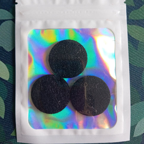 Three black round items in a white pouch with a reflective cover on a green leafy background.