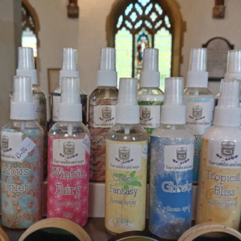 Collection of variously scented room and linen spray bottles in a store setting with decorative elements. Four candles and soaps