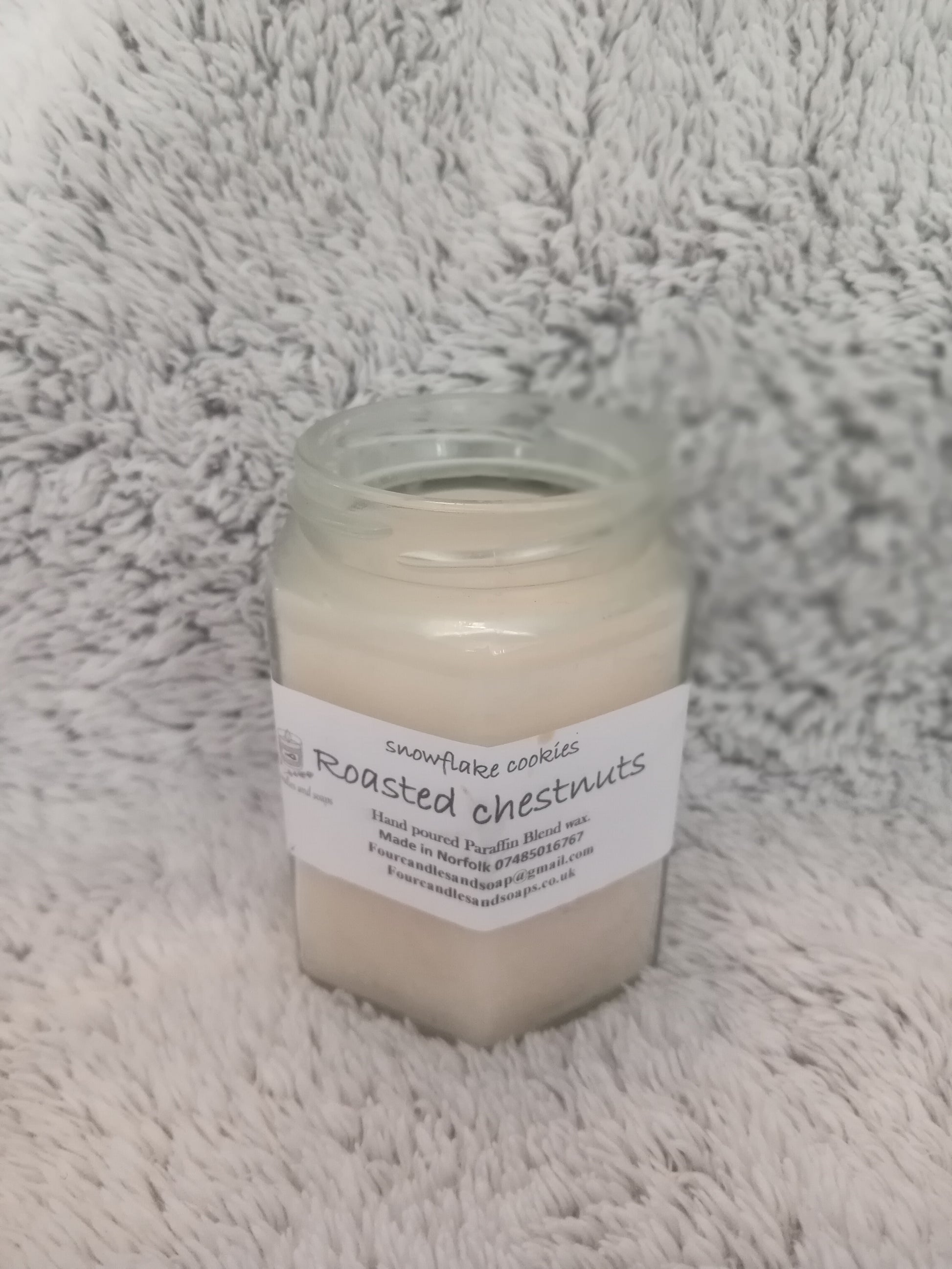 A jar candle with a label that reads 'Roasted Chestnuts' placed on a white furry surface.