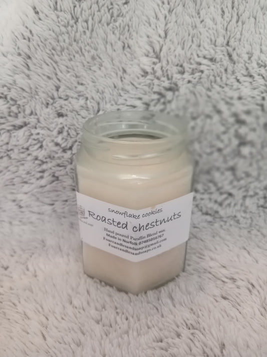 A jar candle with a label that reads 'Roasted Chestnuts' placed on a white furry surface.