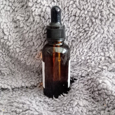 Amber glass dropper bottle with black cap on a textured gray surface with Invictus beard oil