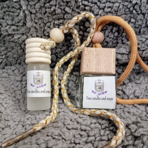 Two small car diffuser containers with labels on a textured grey surface Four Candles and Soaps