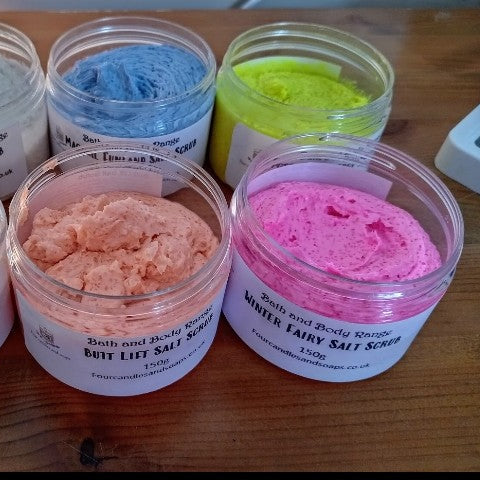Multiple jars of body salt scrub with various colors such as clear, pink, blue, green, beige, and yellow. four candles and soaps